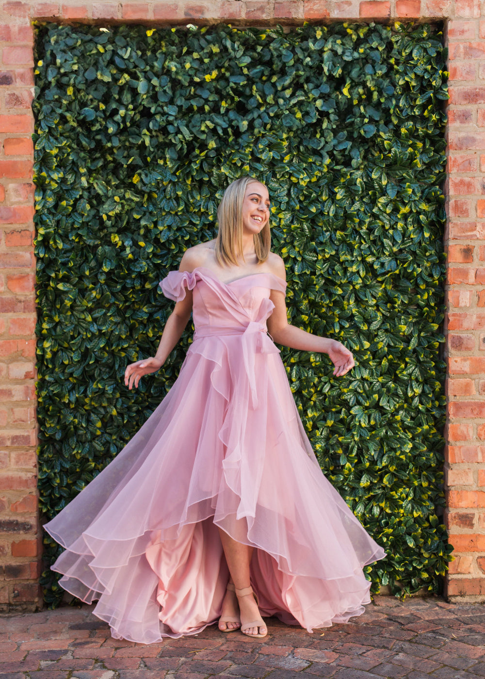 Woman in a pink dress standing against a green leafy wall.