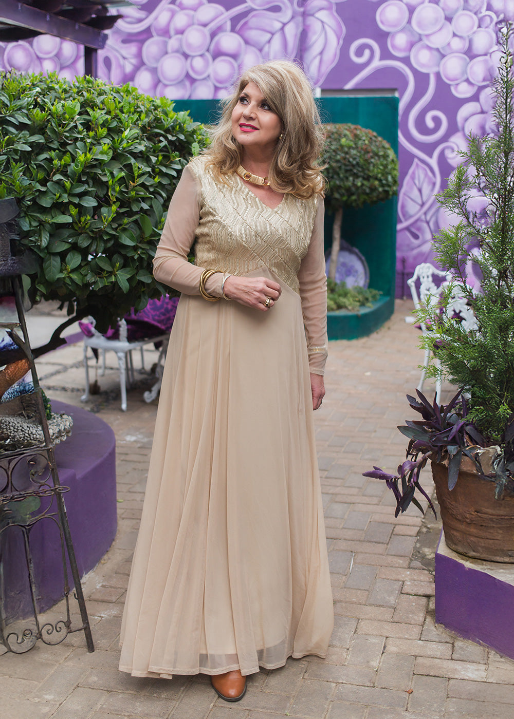 Woman in a beige dress standing in front of a purple floral wall.